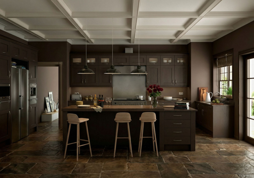 A warm, modern kitchen with dark wood cabinets, a large central island, and three light wooden bar stools. Three industrial pendant lights hang above the island, which is topped with wine bottles, glasses, plates, books, and a vase of red flowers. Stainless steel appliances line the back wall, and a window on the right lets in natural light with greenery visible outside. The floor is made of large rustic stone tiles, adding texture to the space.