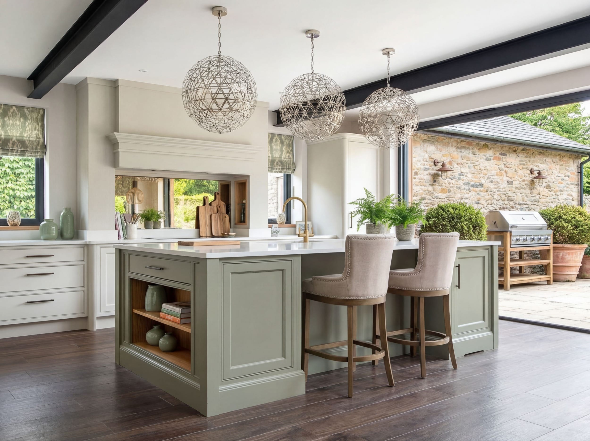 Bespoke painted shaker kitchen in a Yorkshire home featuring a large central island with seating, white quartz worktops, brass tap, open shelving, and three sculptural pendant lights beneath exposed ceiling beams, with wide sliding doors opening onto a stone patio.