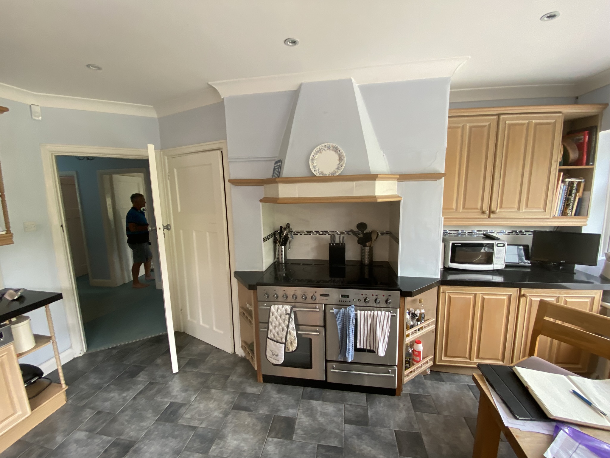 L-shaped kitchen with pale green shaker cabinets, contrasting wood trim, white worktops, and green splashback tiles