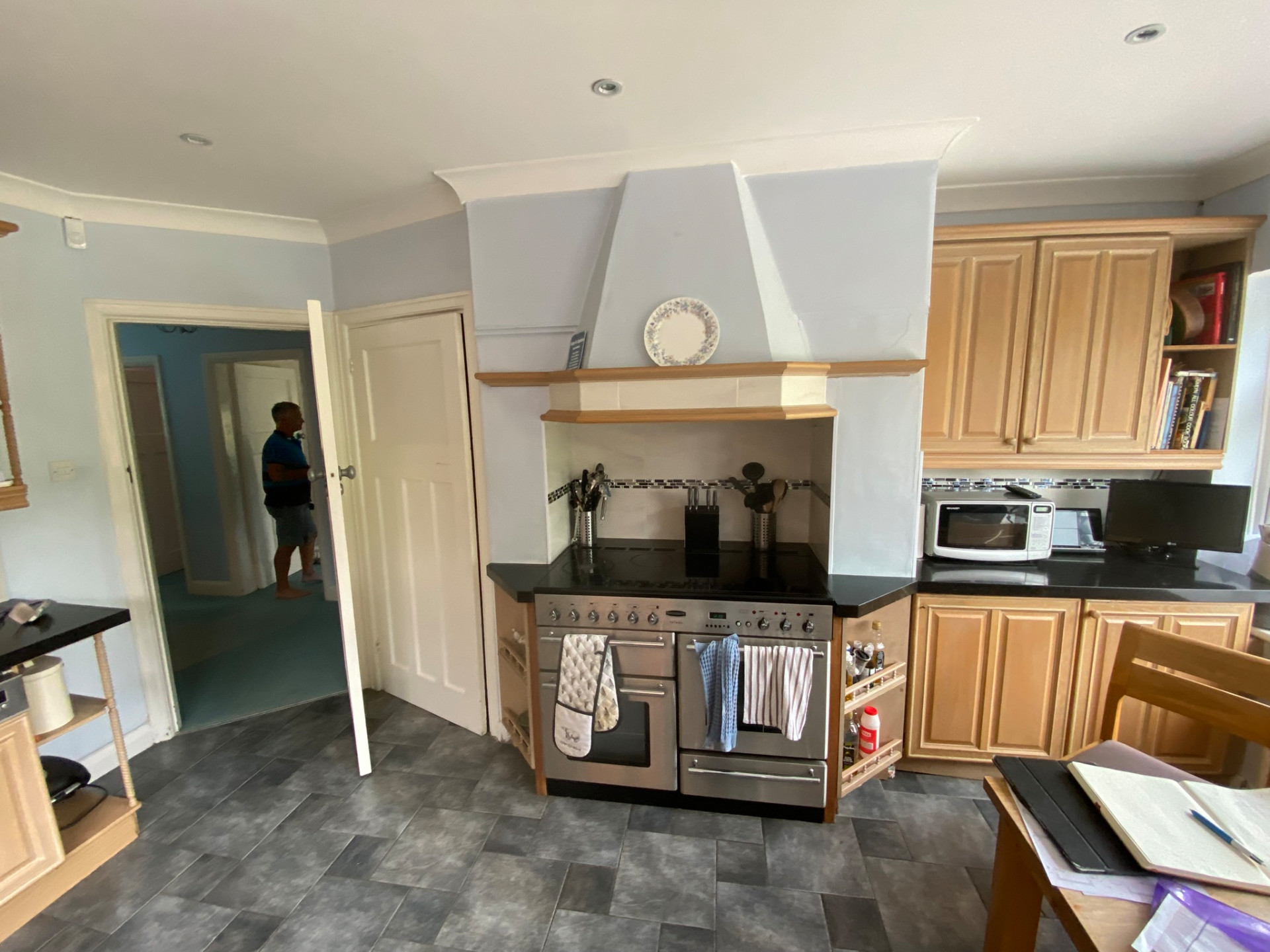 Maree Before L-shaped kitchen with pale green shaker cabinets, contrasting wood trim, white worktops, and green splashback tiles