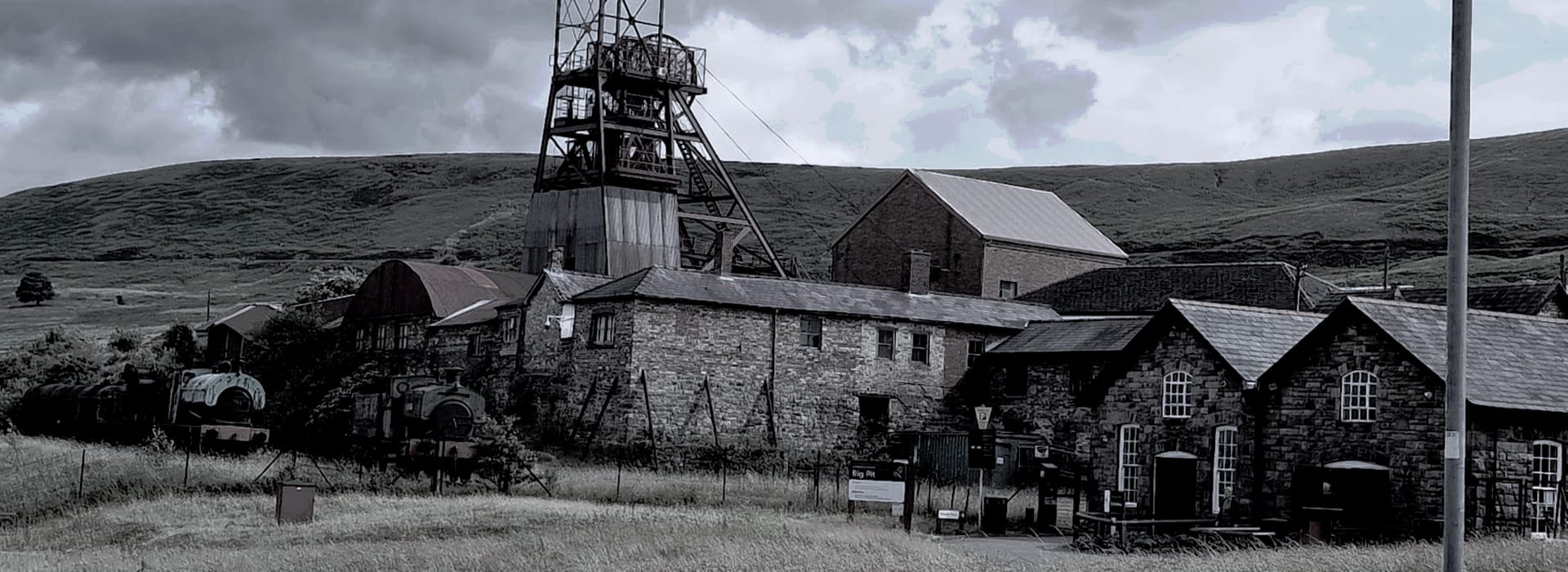 industrial mining site with stone buildings and metal headframe under cloudy sky