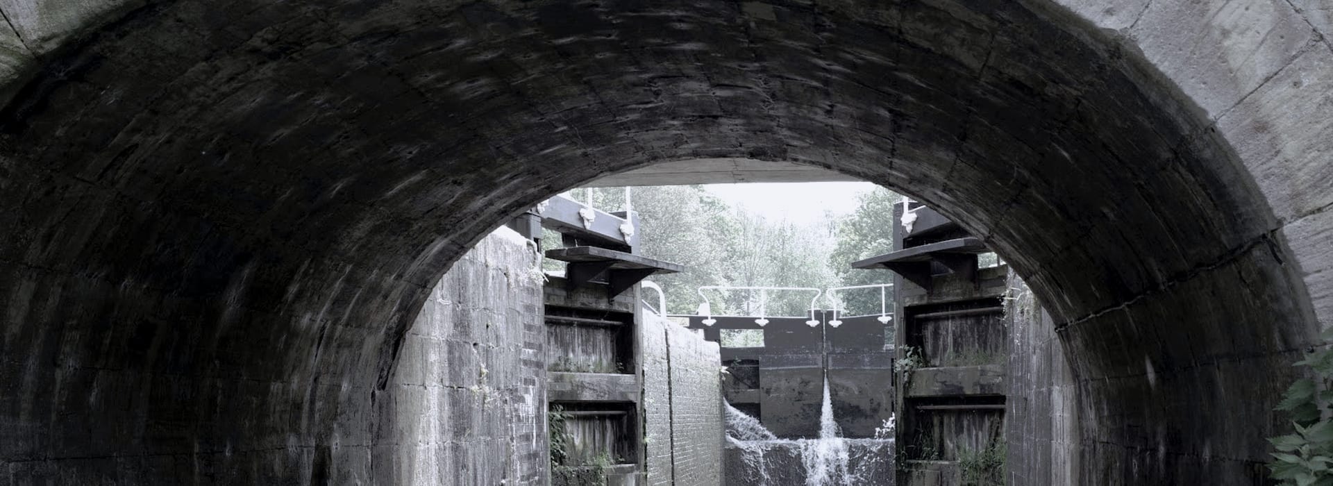 Stone tunnel framing a canal lock gate with water flowing through