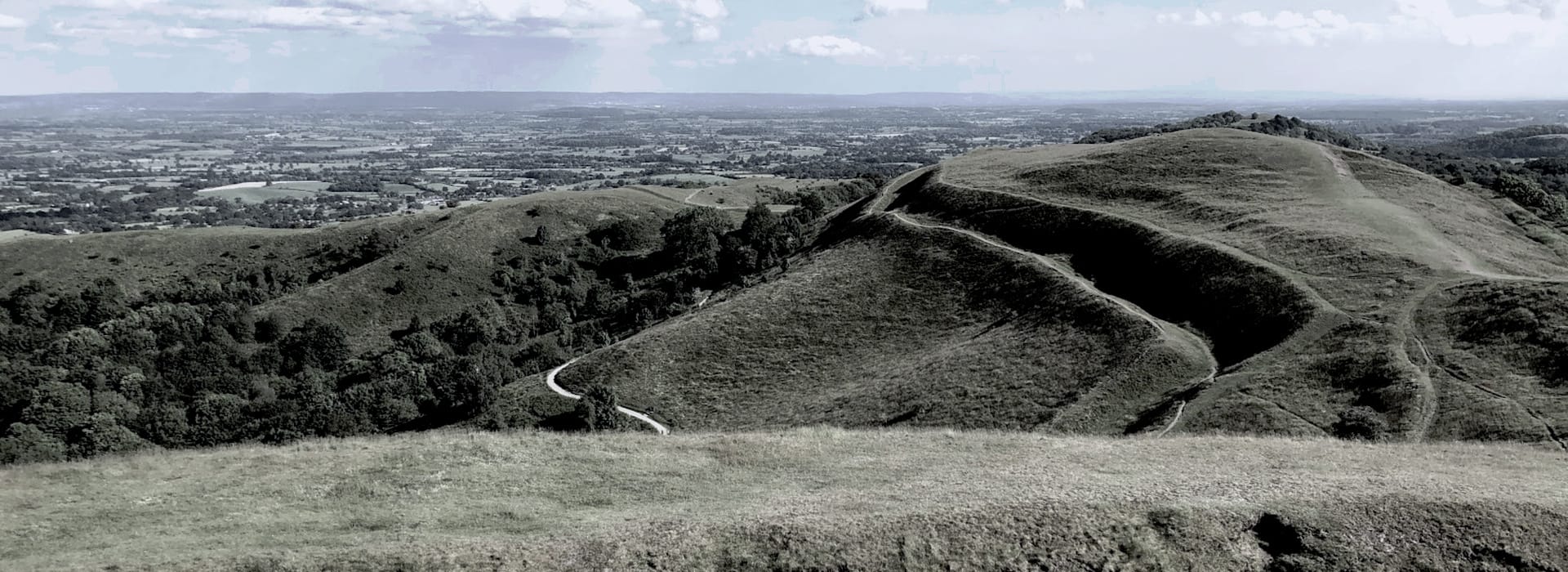 rolling green hills with winding footpaths under cloudy sky