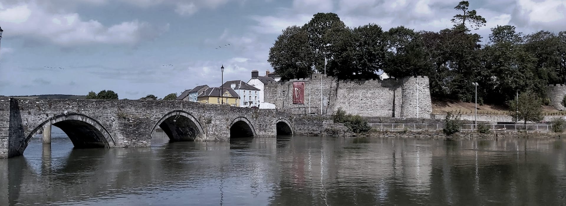 arched stone bridge over river with castle walls and trees behind