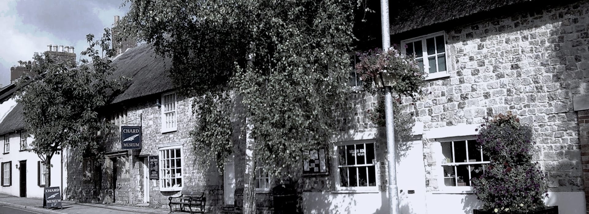 stone building with thatched roof, white-framed windows and leafy trees outside