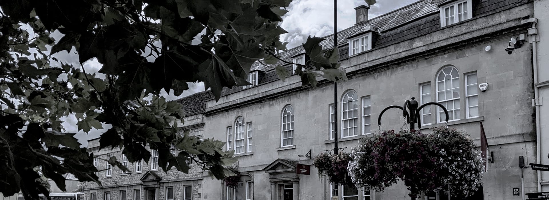 Bespoke Kitchens Chippenham - Mastercraft Kitchens stone building with arched windows and hanging flower baskets, leafy branches in foreground