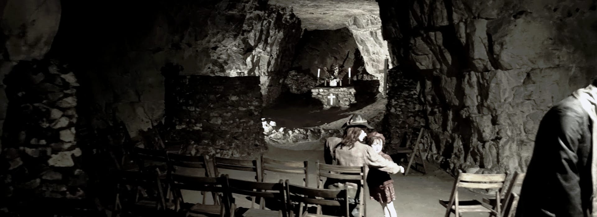 dimly lit stone cave with wooden chairs and small altar at the back