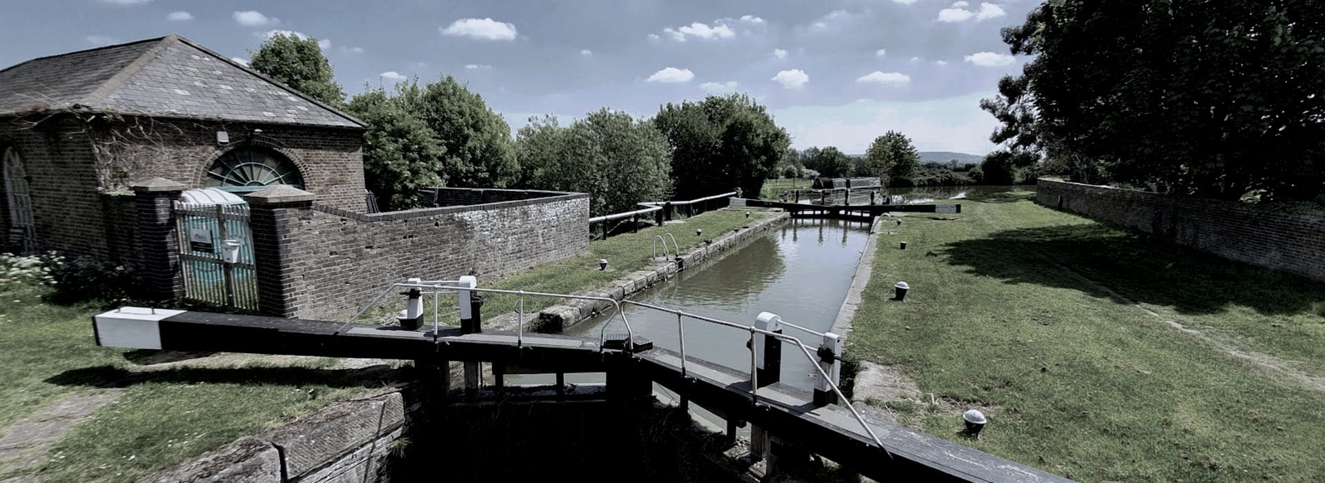 brick lock-keeper's cottage beside canal lock with green grass and trees