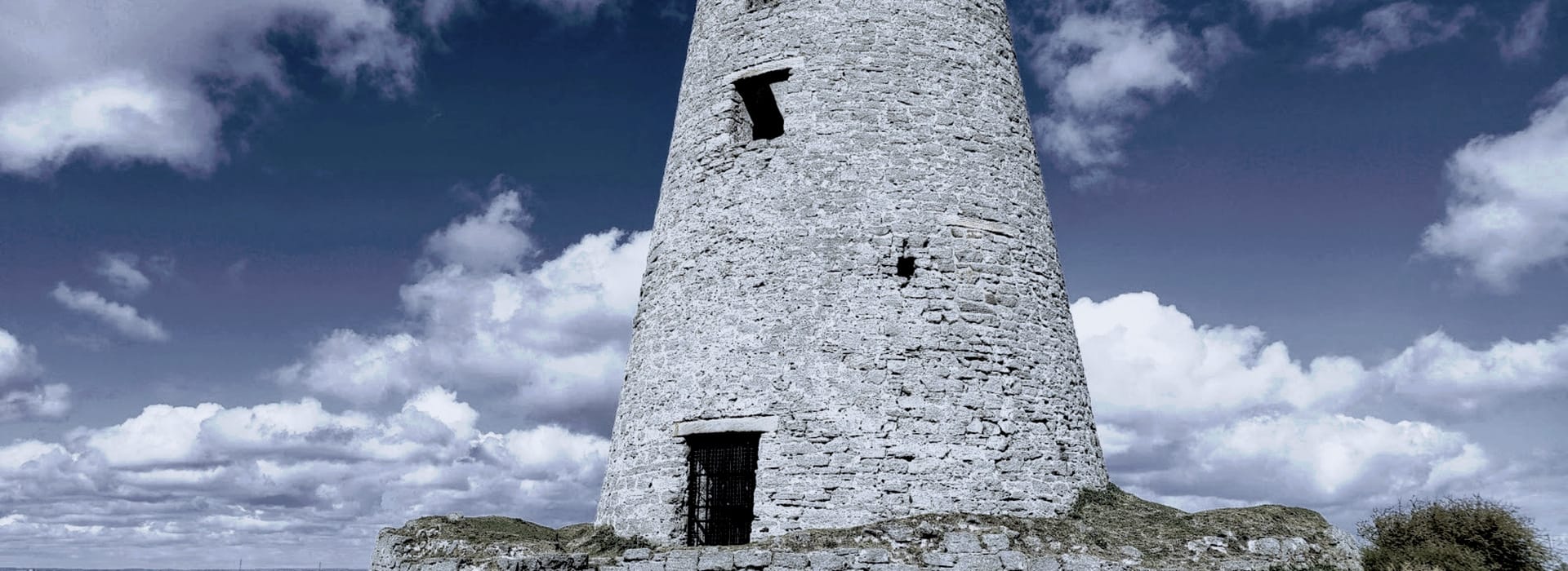 round stone tower with barred doorway against a cloudy blue sky