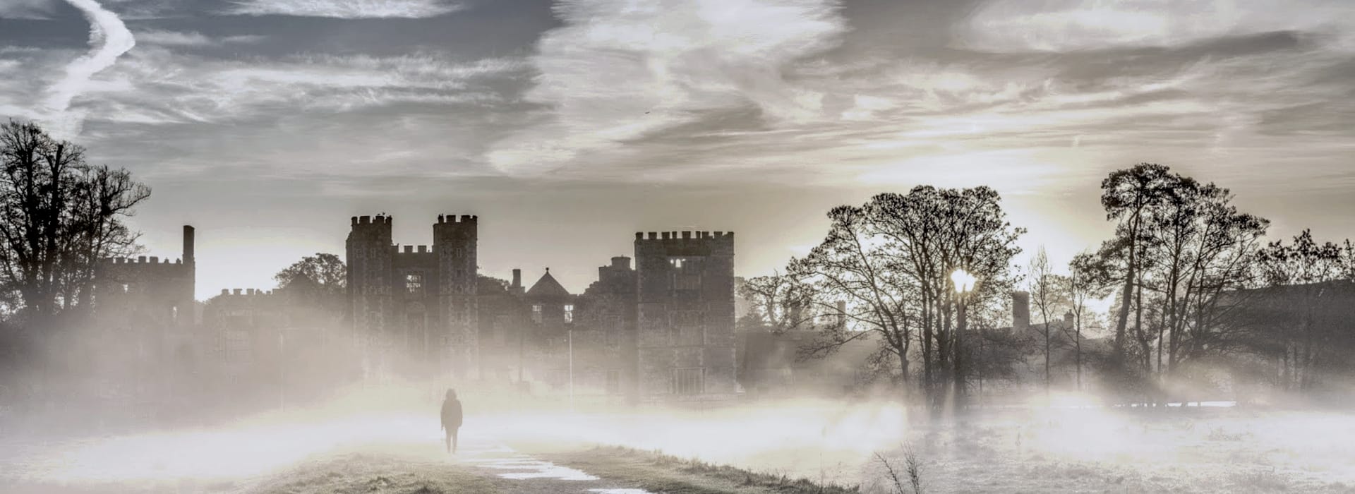 misty castle silhouette at sunrise with lone figure walking on path