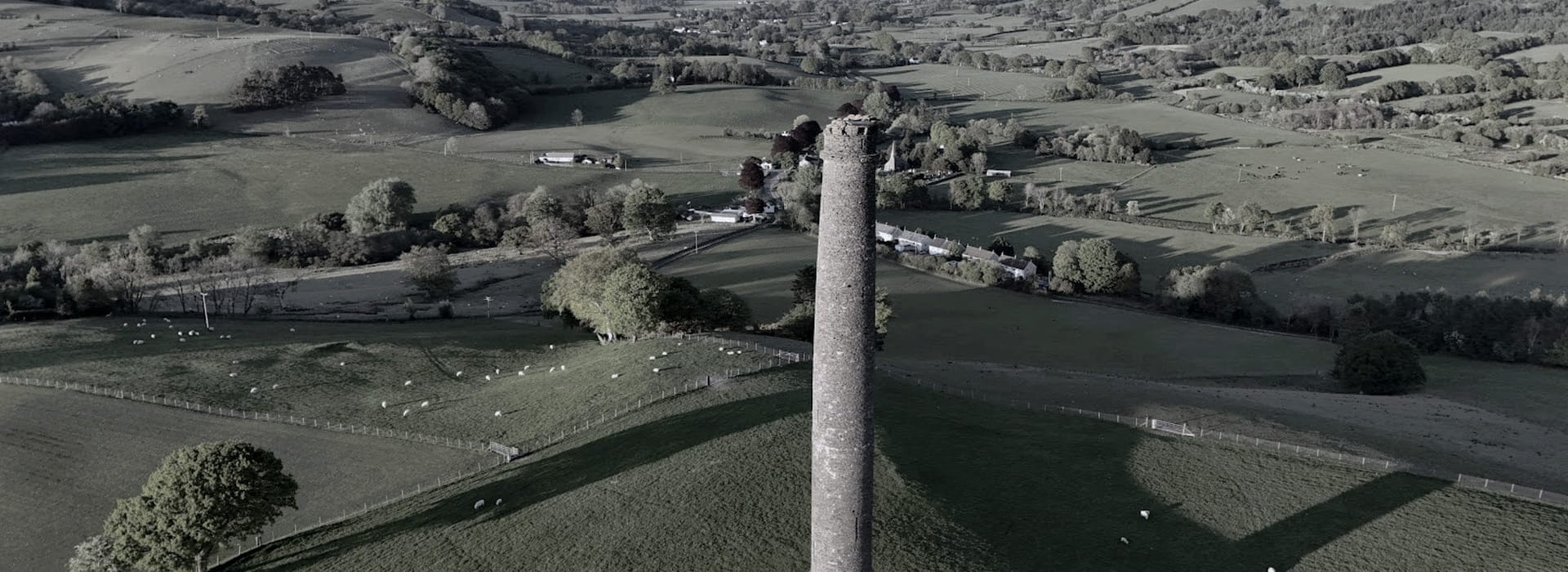 tall stone tower rising from green rolling countryside with scattered sheep