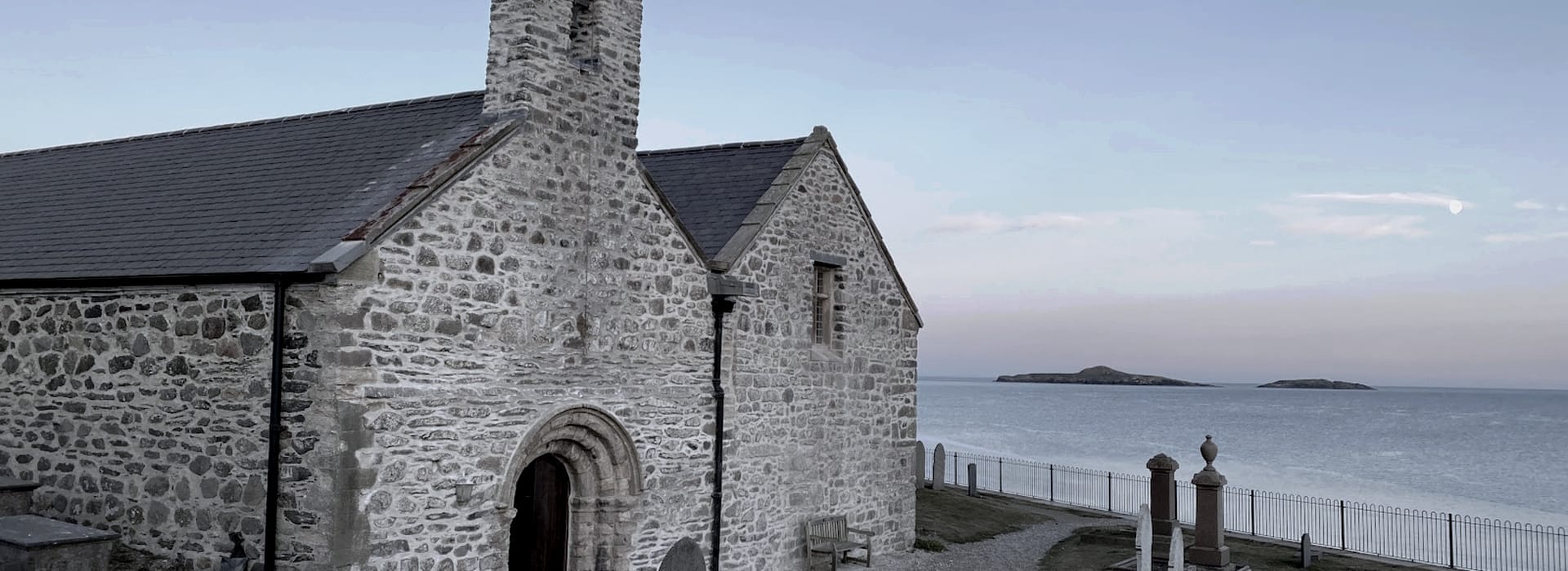 stone church with arched doorway overlooking calm sea and distant islands