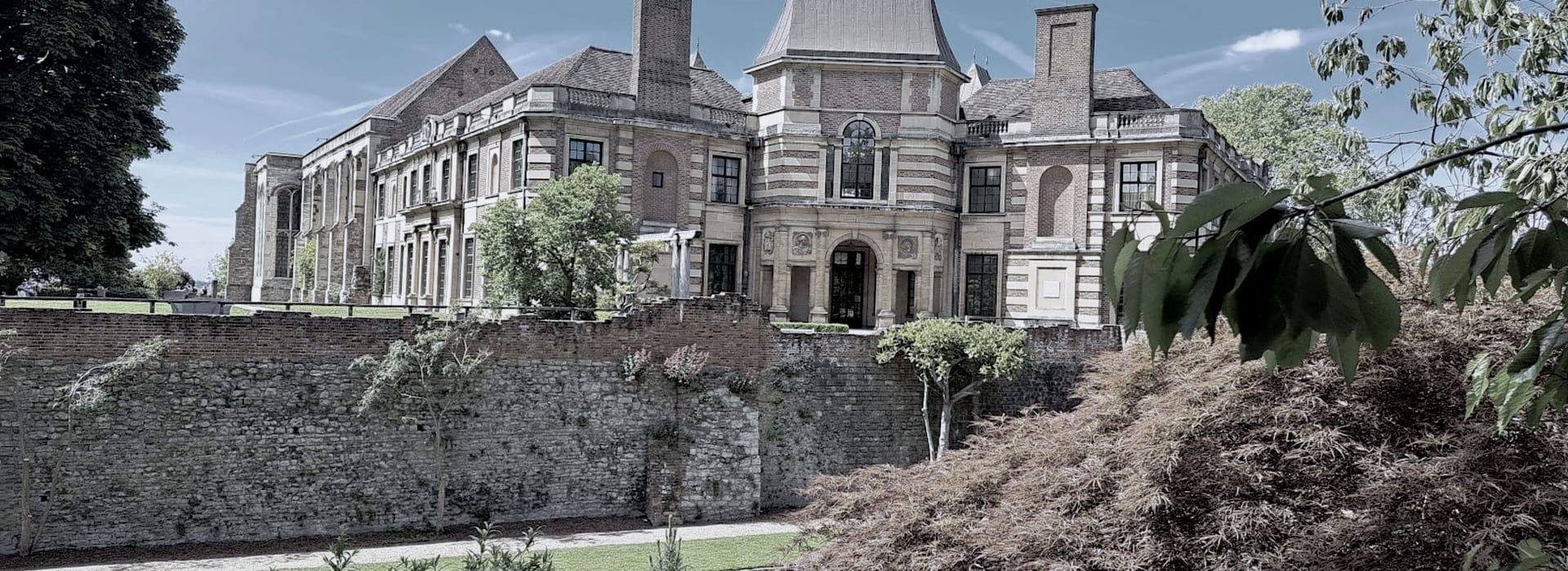 historic mansion with striped brickwork, arched entrance and stone wall in foreground