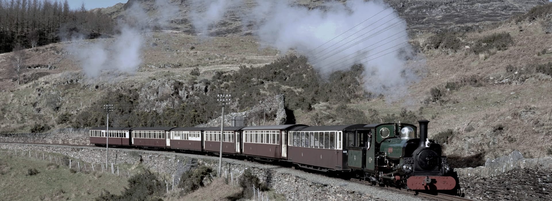 vintage steam train with maroon carriages curving through rocky countryside