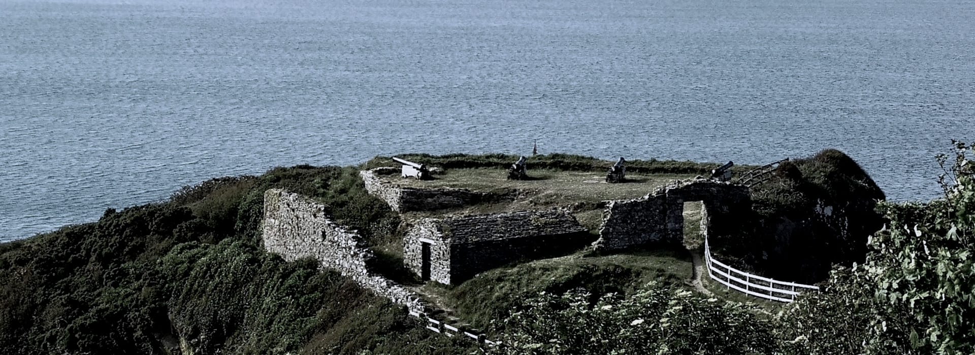 weathered stone fort with cannons overlooking the sea, surrounded by greenery