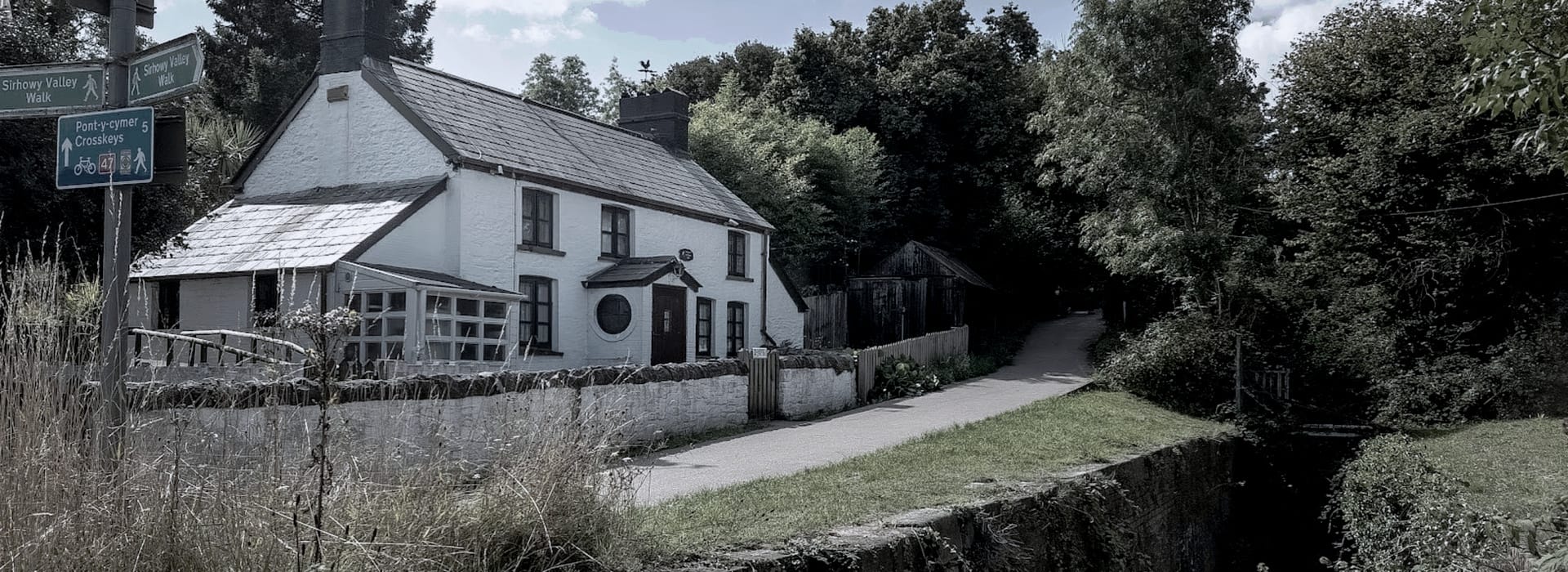 White cottage with slate roof beside a leafy canal path