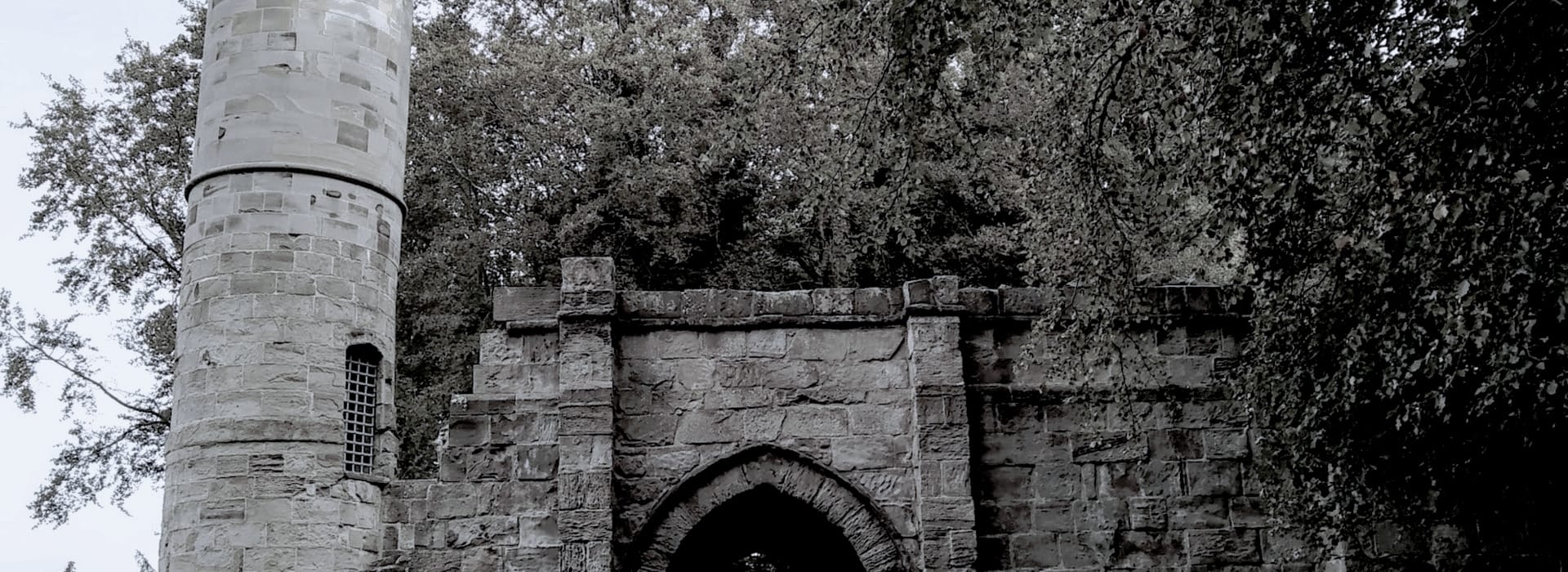 stone archway with round tower, surrounded by dense green trees