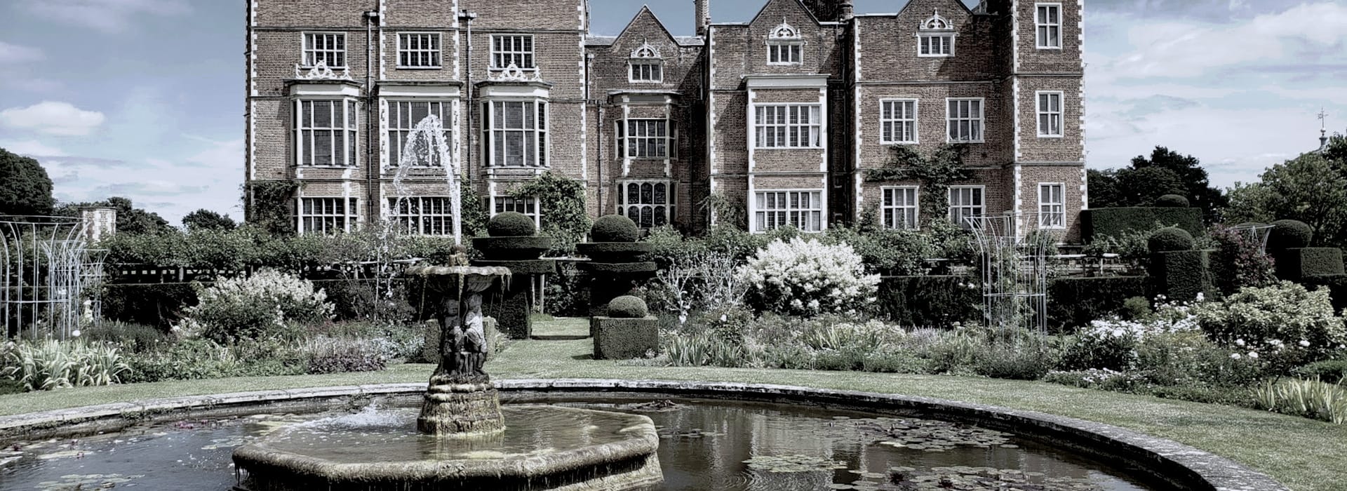 historic brick manor house with bay windows, formal garden and central stone fountain