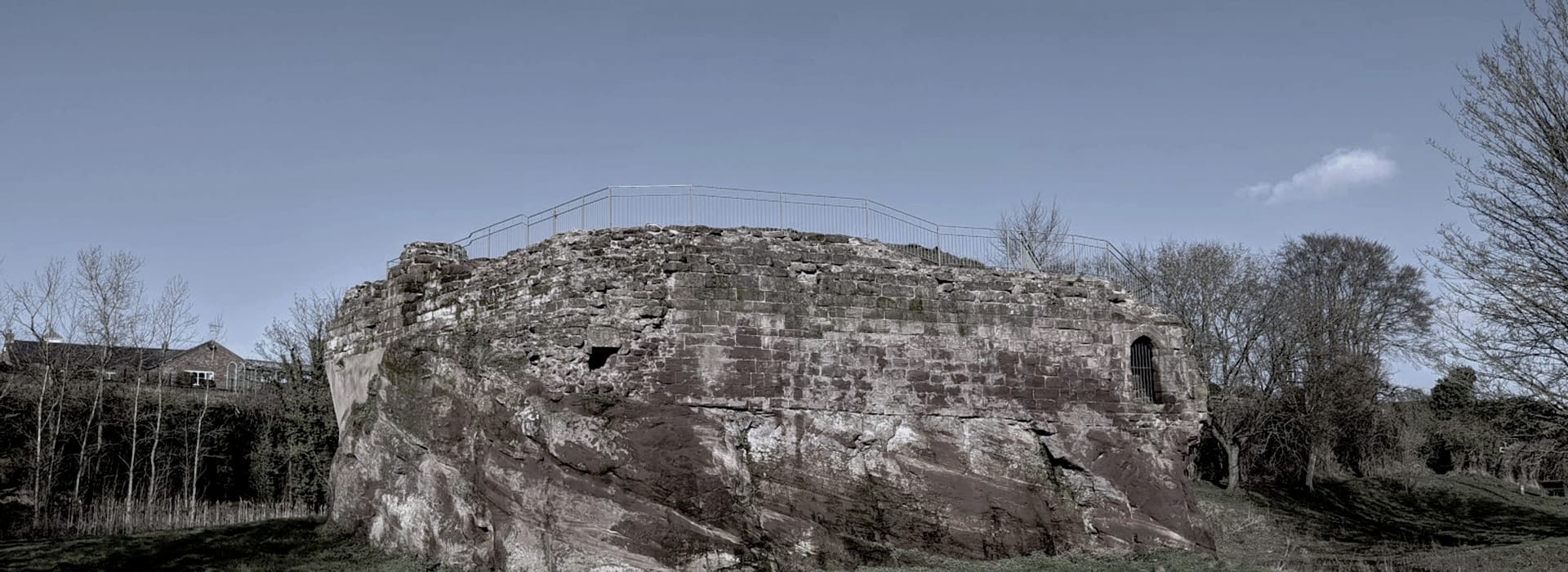 weathered stone ruin with metal railings on top, surrounded by bare trees