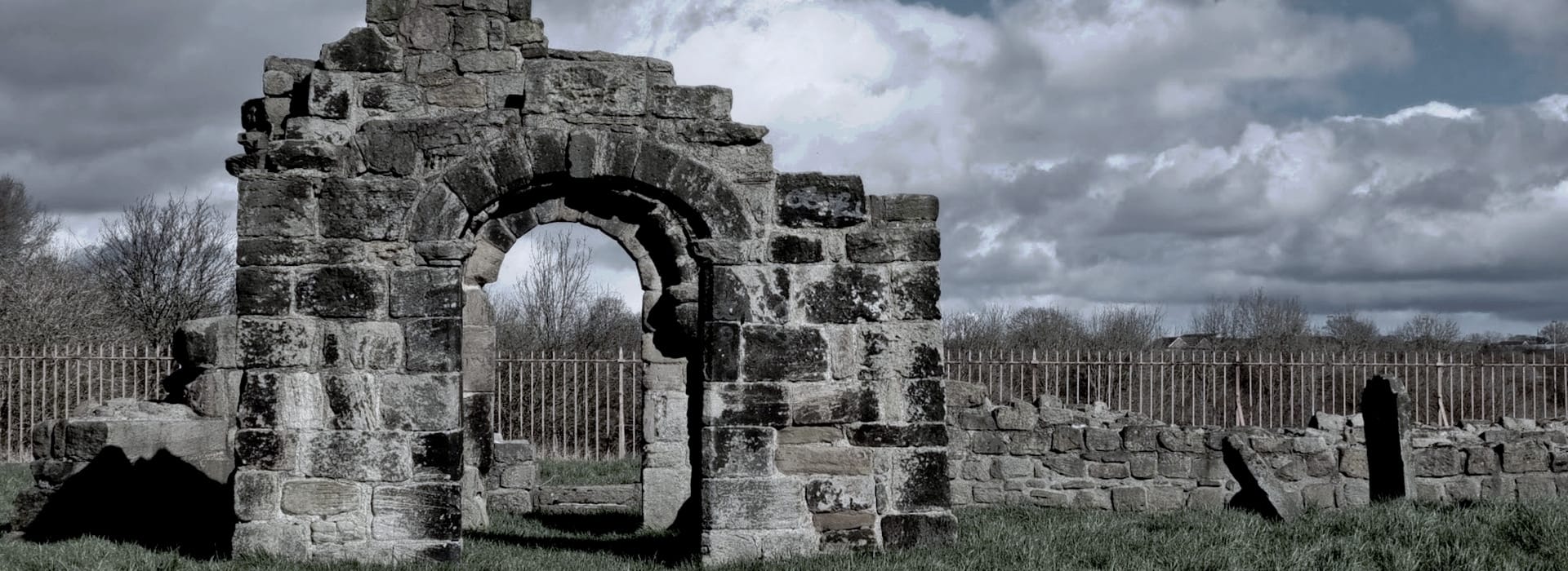 weathered stone archway ruins with cloudy sky and iron fence background