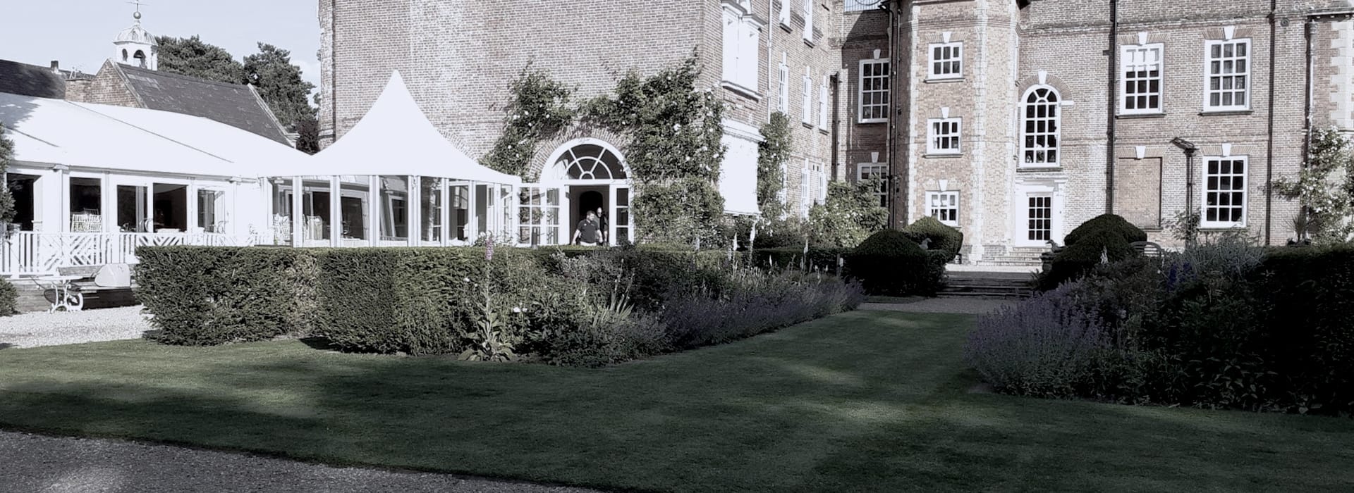 historic brick building with white marquee and manicured garden hedges