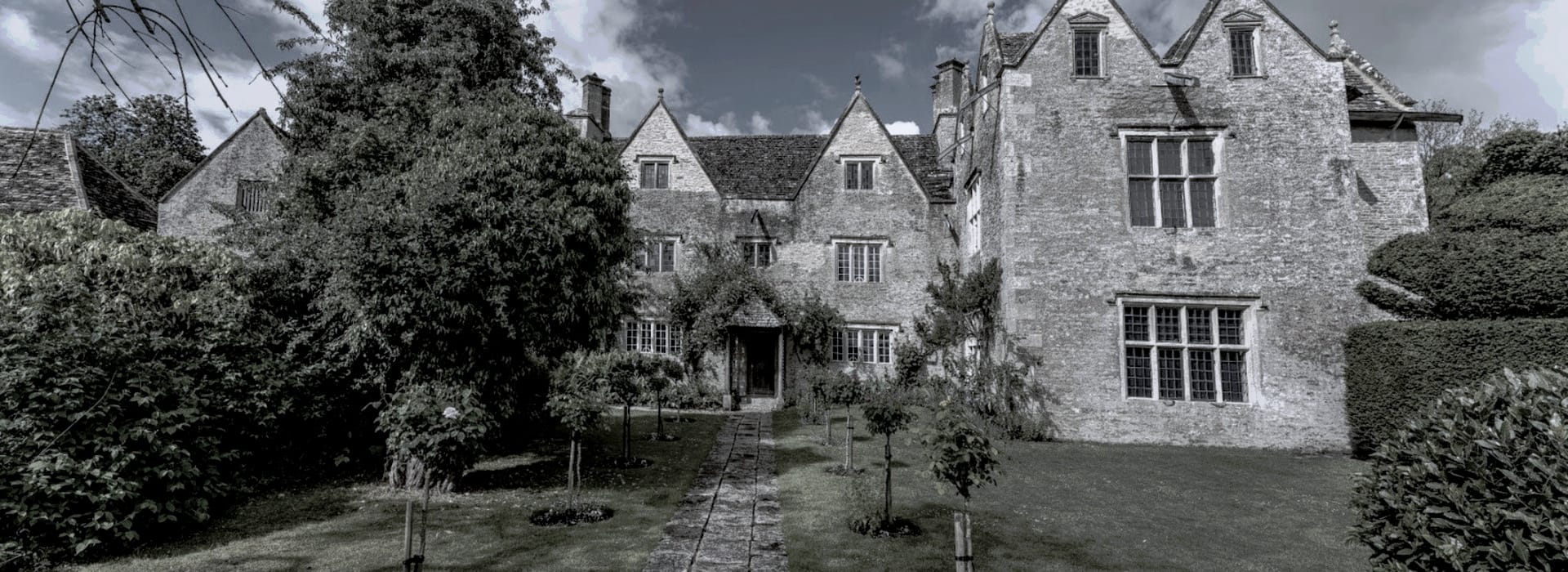Stone manor house with steep gables, tall chimneys and manicured front lawn