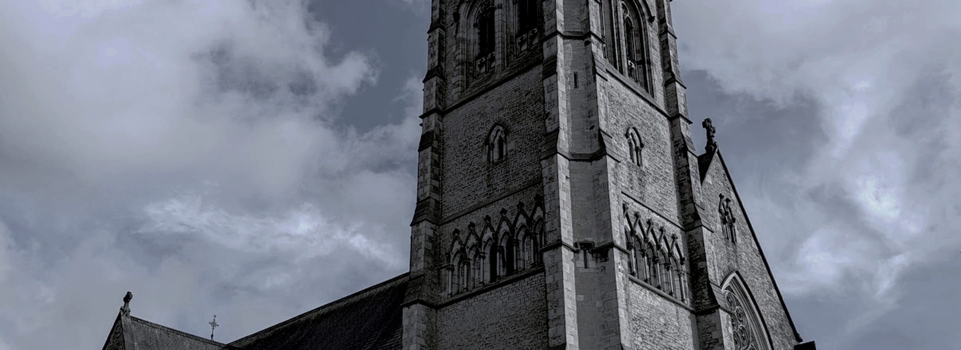 grey stone church tower with pointed arches against cloudy sky