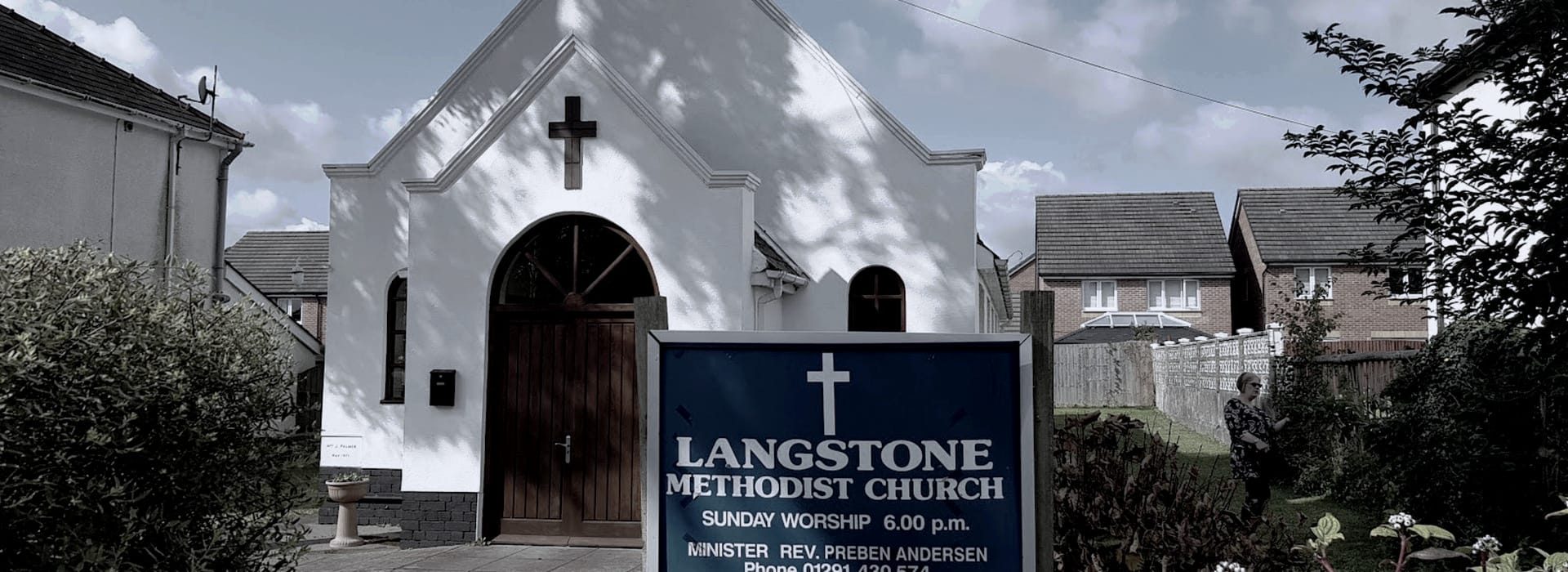 white chapel with arched windows and dark wooden door, blue sign in foreground