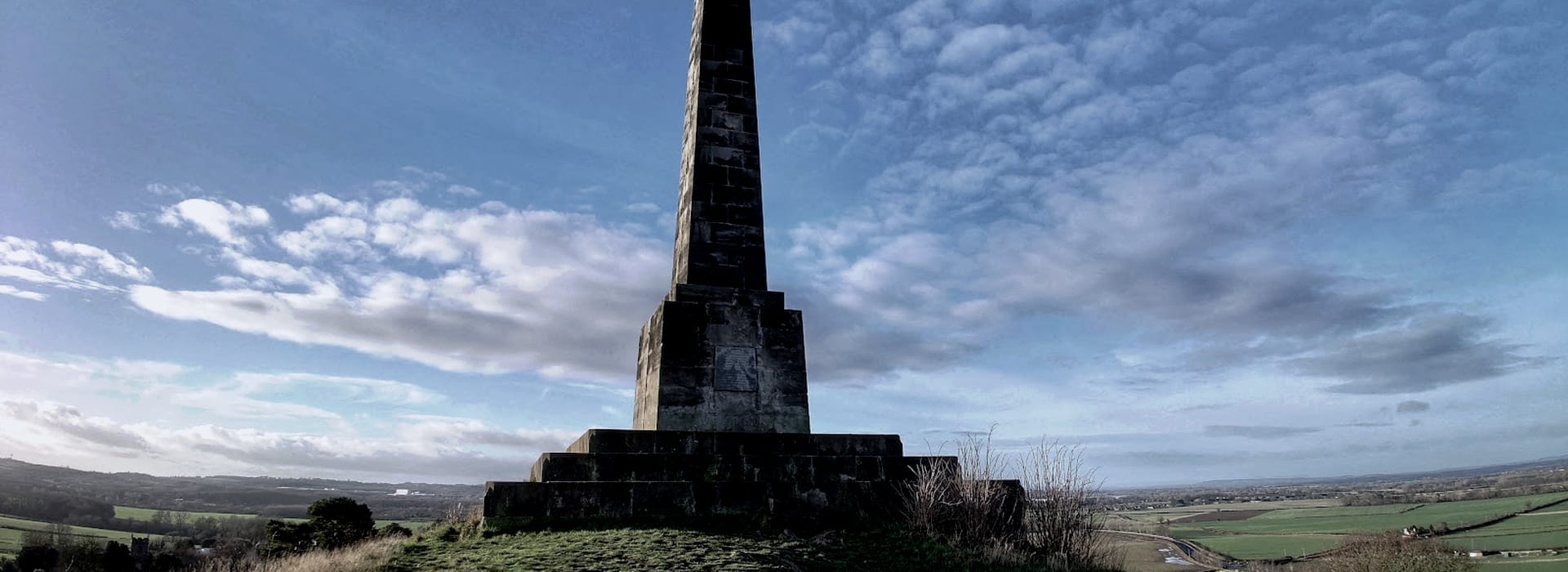 stone obelisk monument on stepped base with wide sky and green landscape