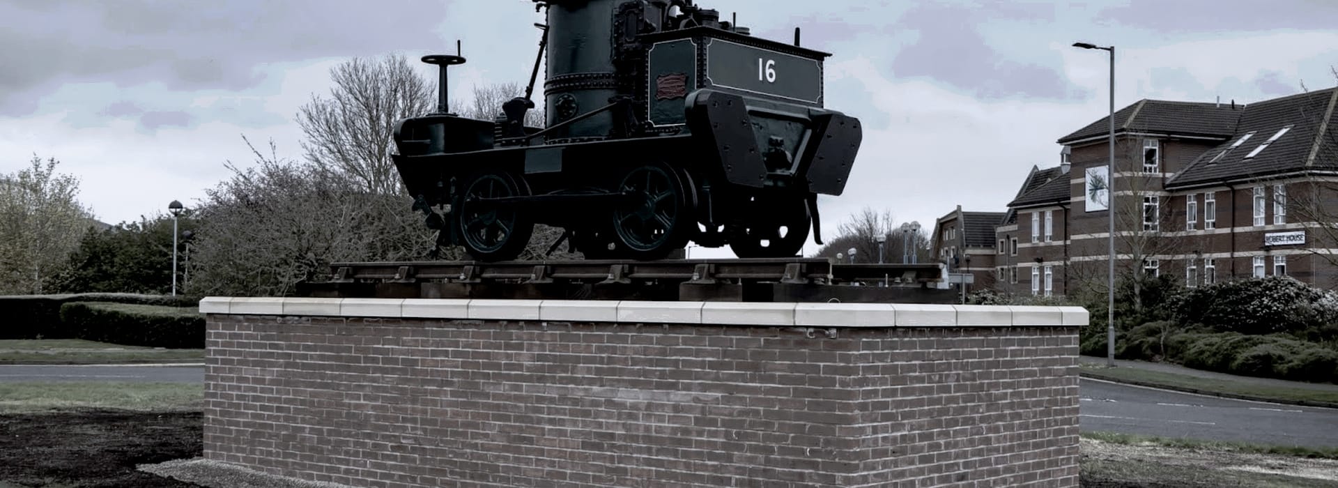 black vintage locomotive on raised brick plinth beside modern buildings