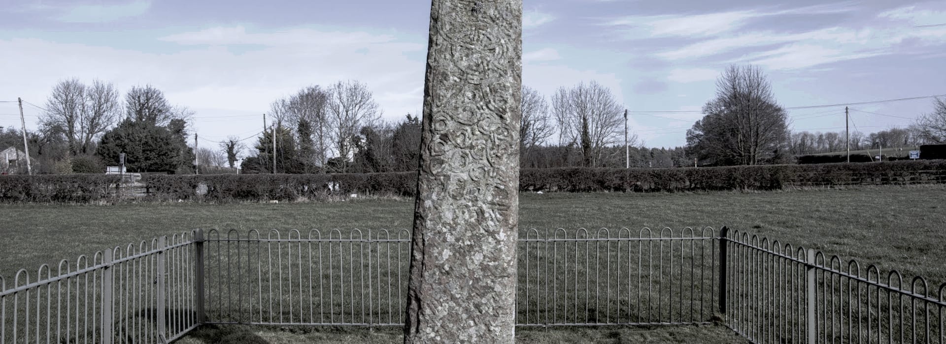 Tall weathered stone pillar with intricate carvings, surrounded by metal railings