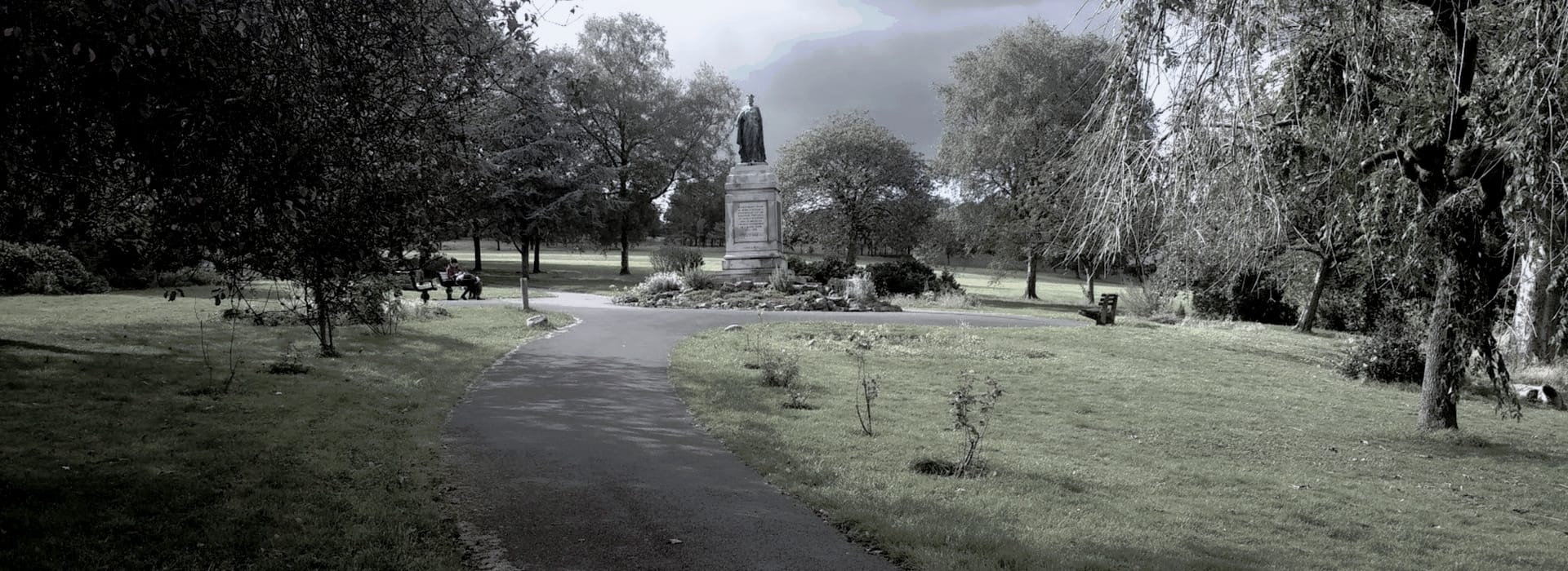 statue on plinth surrounded by trees and winding path in park