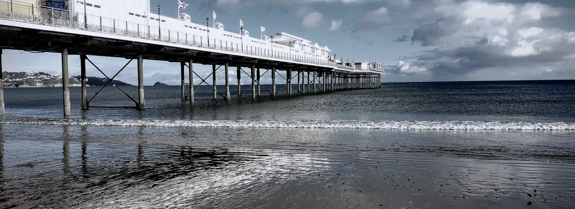 long white pier with flags over calm blue sea and wet sand