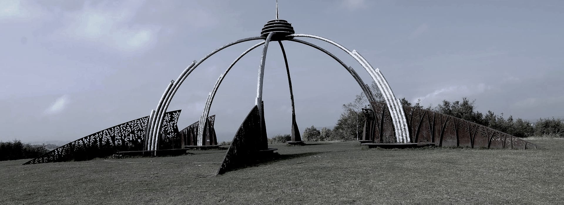 large outdoor metal sculpture with curved silver arches and patterned rust panels
