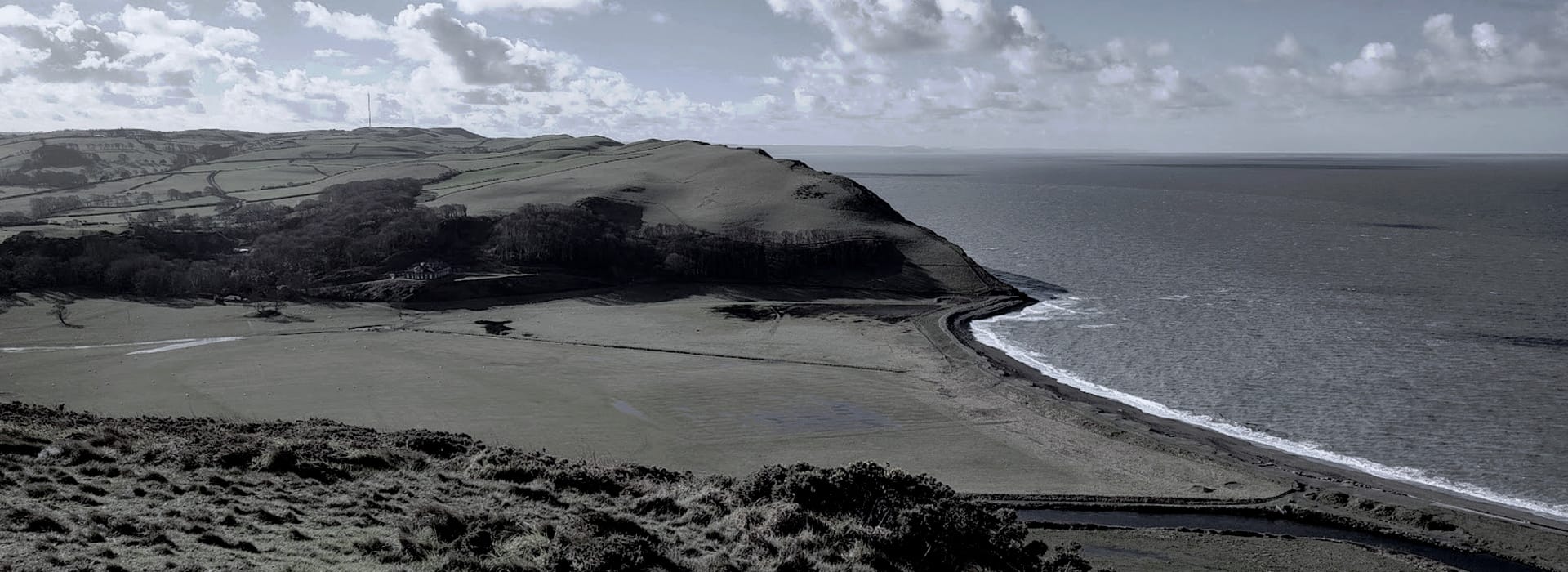 coastal hillside with patchwork green fields and curved shoreline meeting the sea
