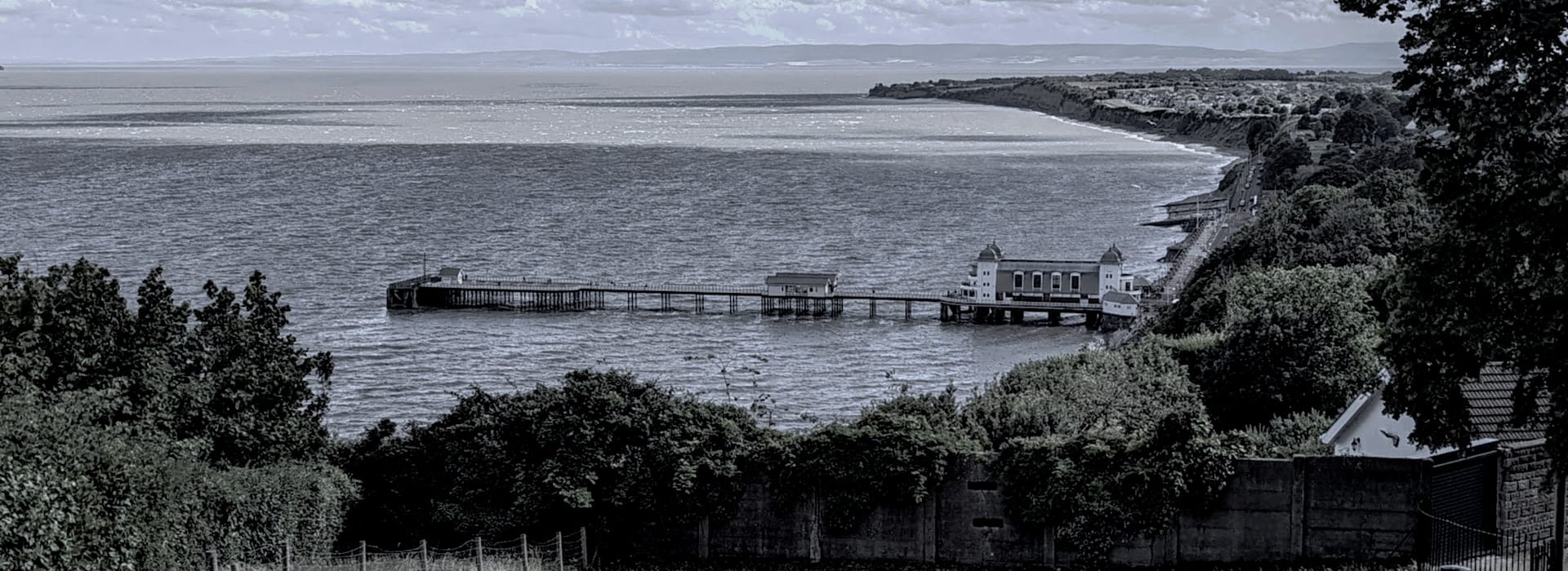long pier stretching into grey sea with green trees in foreground