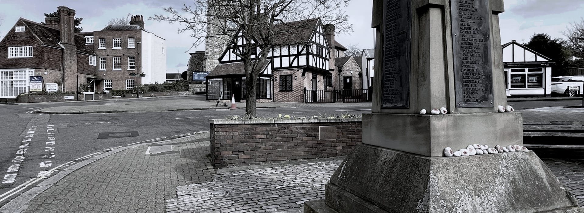 stone war memorial with painted pebbles, Tudor-style buildings in background