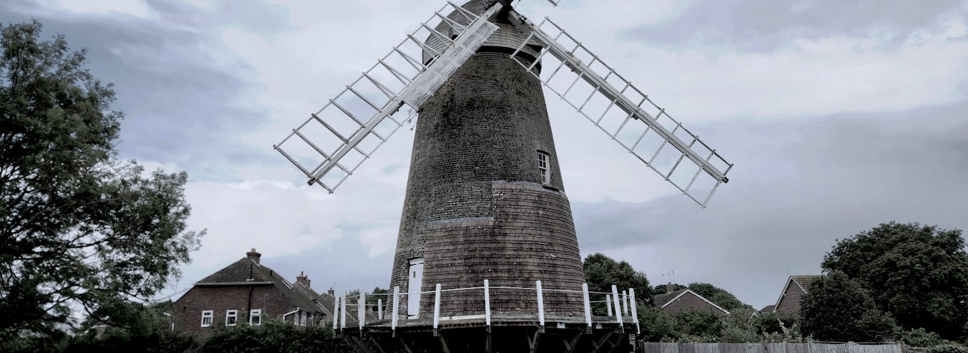 tall brick windmill with white sails against cloudy sky