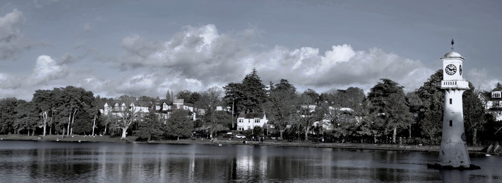 monochrome lakeside scene with tall white clock tower and houses among trees