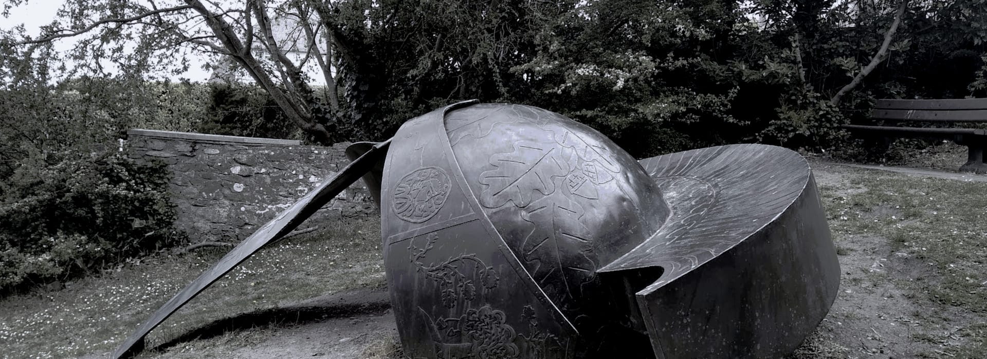 large metallic acorn sculpture with engraved leaf patterns in a park setting