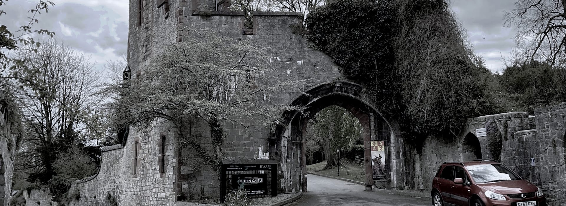 stone castle archway with overgrown ivy and a red car parked nearby