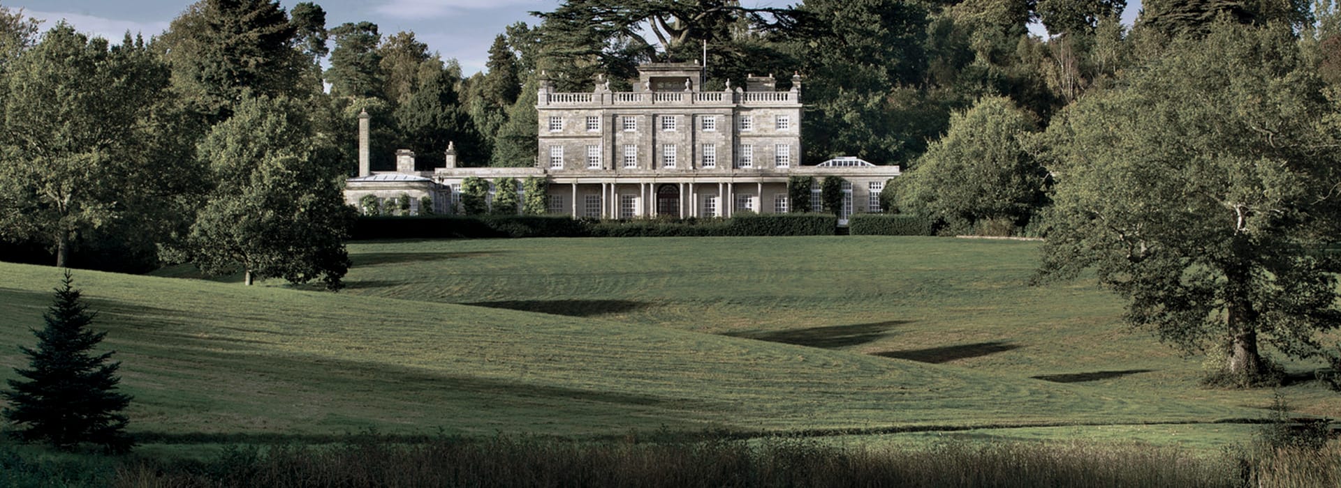 grand stone manor with symmetrical windows set in expansive green grounds