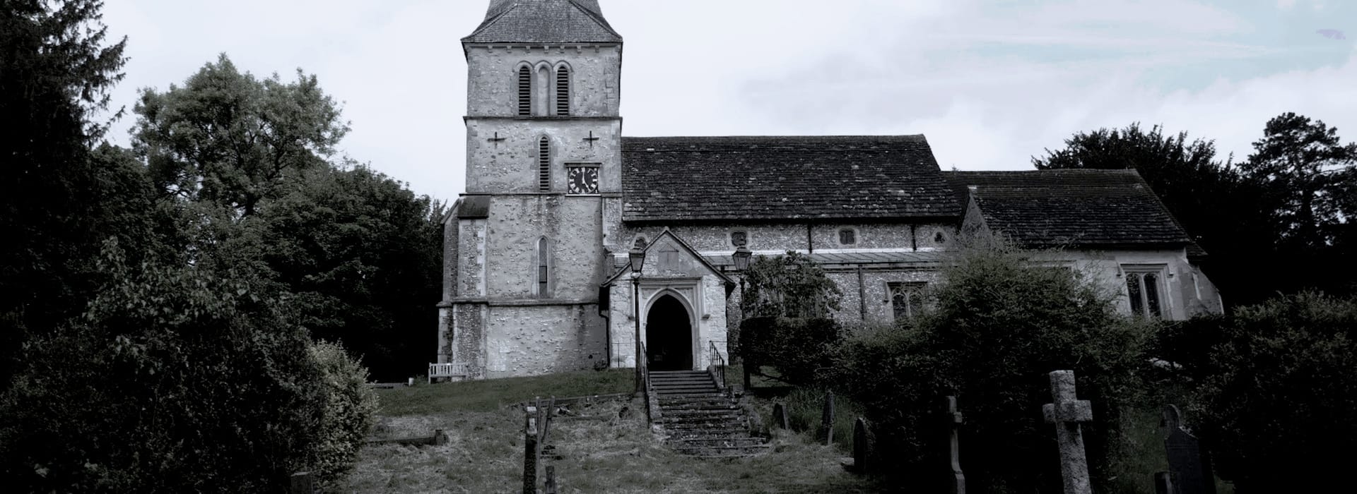 stone church with square tower, arched entrance and overgrown graveyard