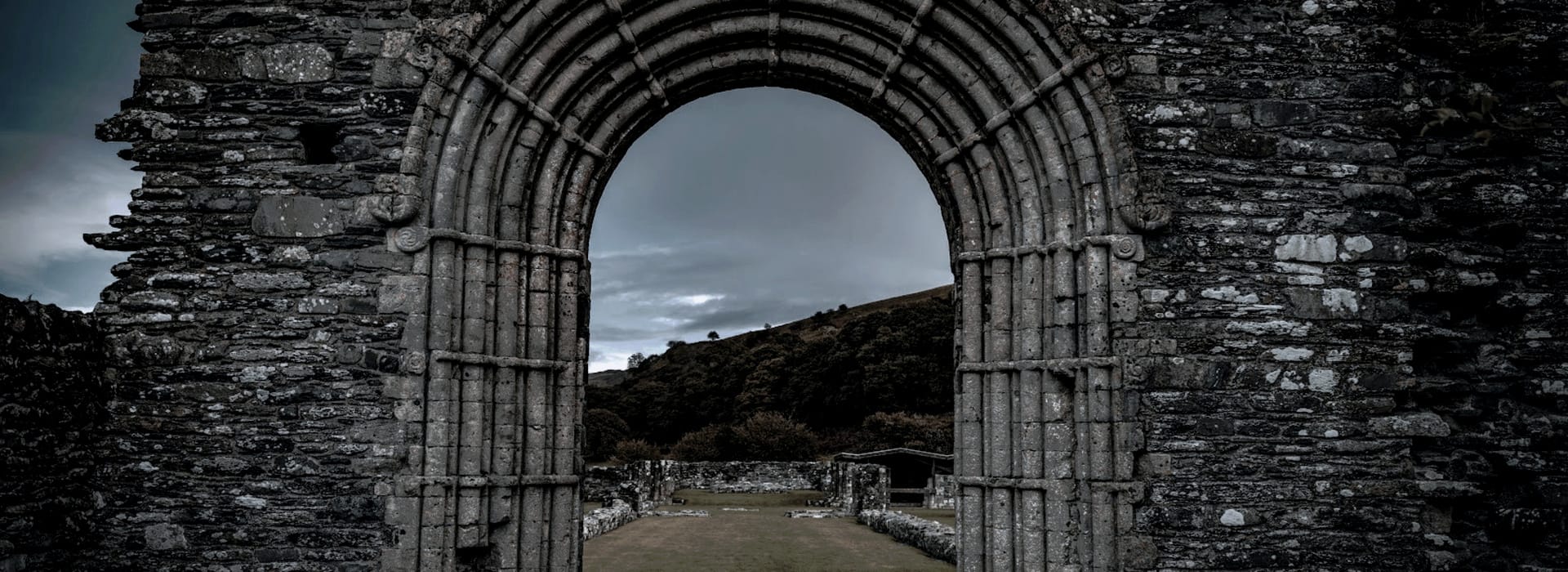 weathered stone archway framing a moody sky and distant hills