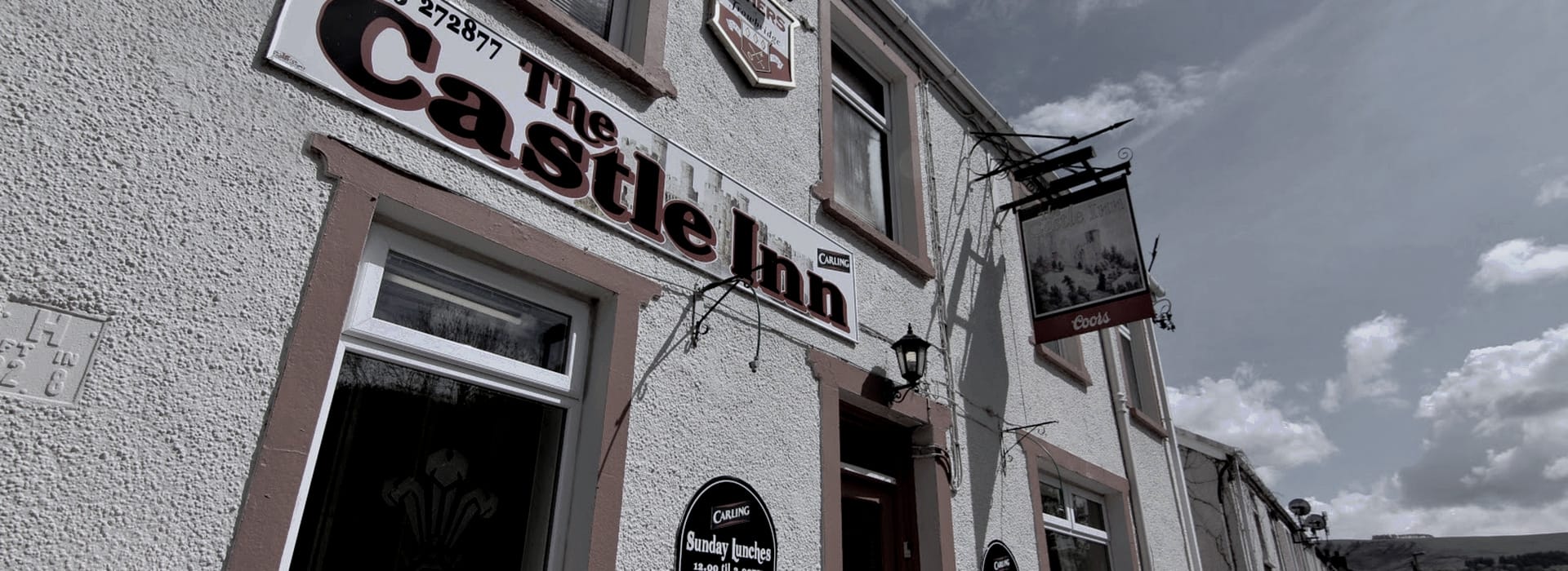 textured white pub exterior with large maroon sign and hanging lantern