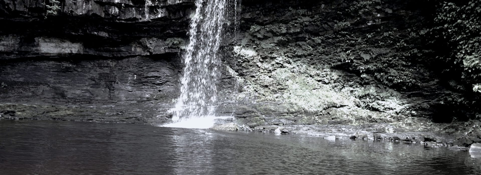 vertical waterfall cascading over dark rocky cliff into calm pool