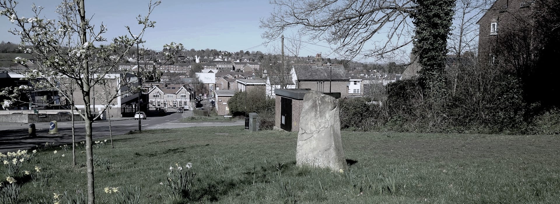 large standing stone on grassy area overlooking town buildings