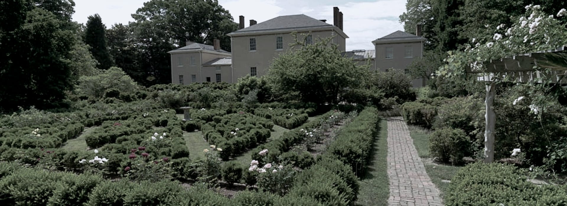 formal garden with geometric hedges, rose bushes and brick path, manor house behind