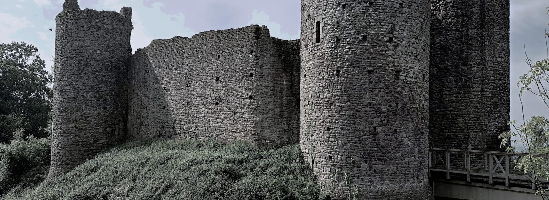 weathered stone castle ruins with round towers and wooden bridge
