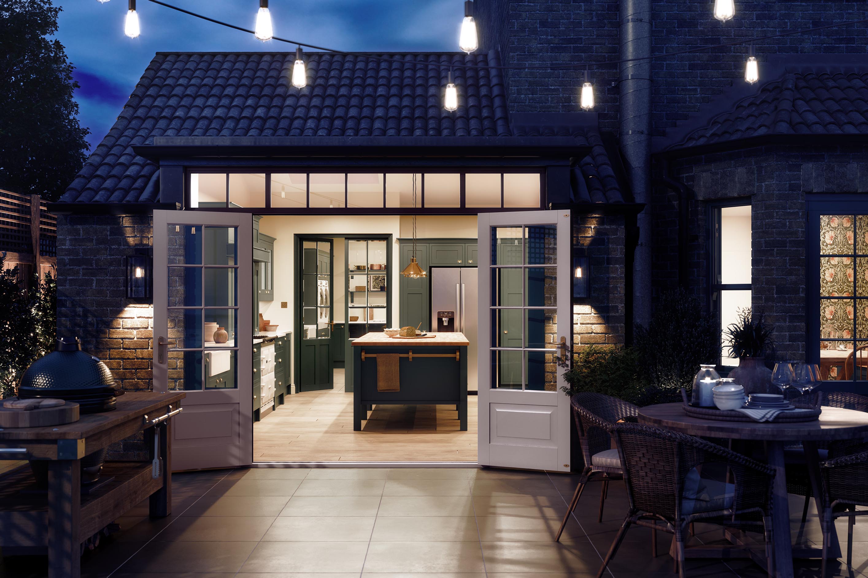 Dark green shaker kitchen with a central island and wooden worktop, viewed from a patio at dusk